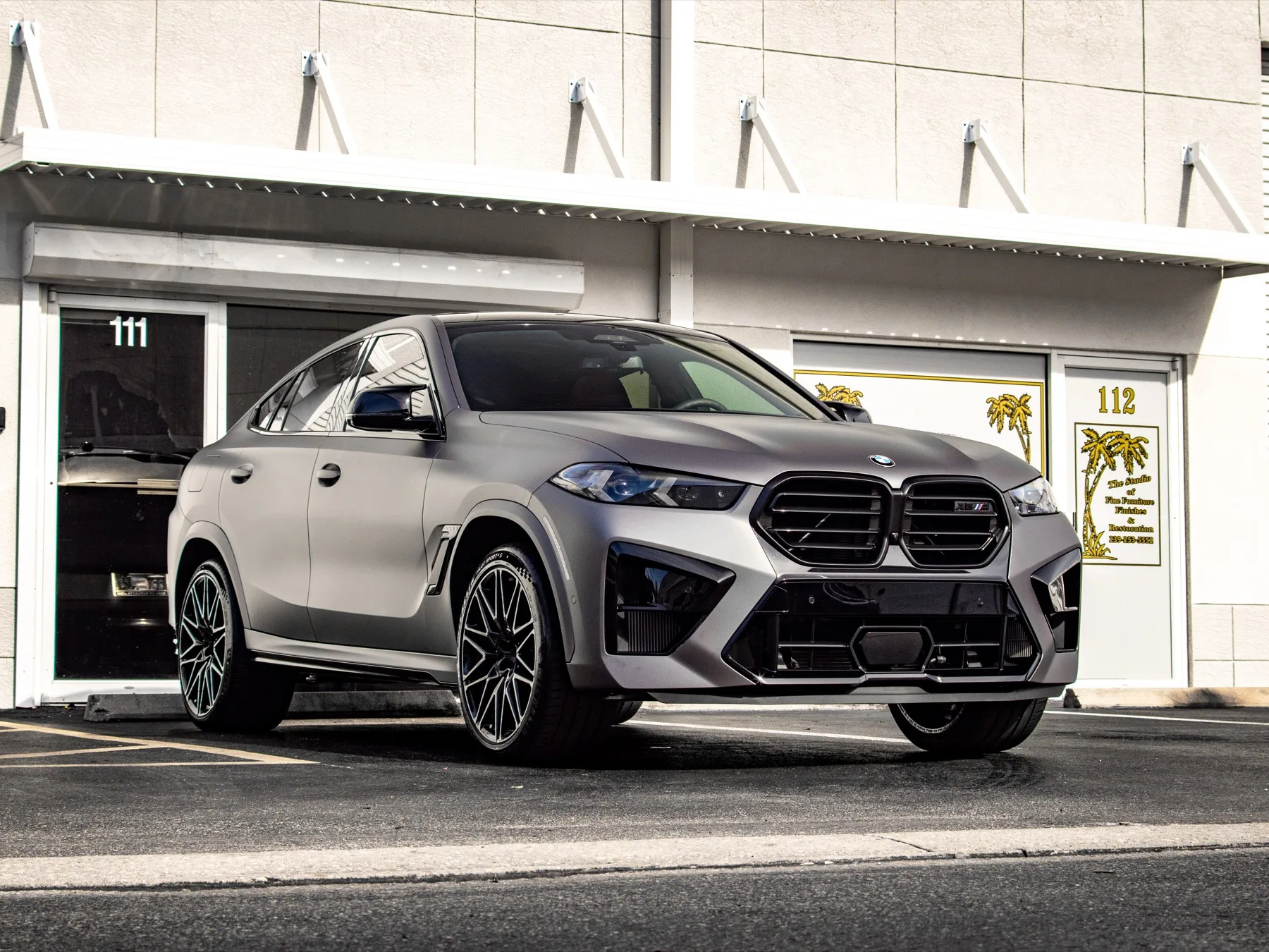2026 BMW X6 M Competition in matte dark gray vinyl wrap, front three-quarter view outside the studio
