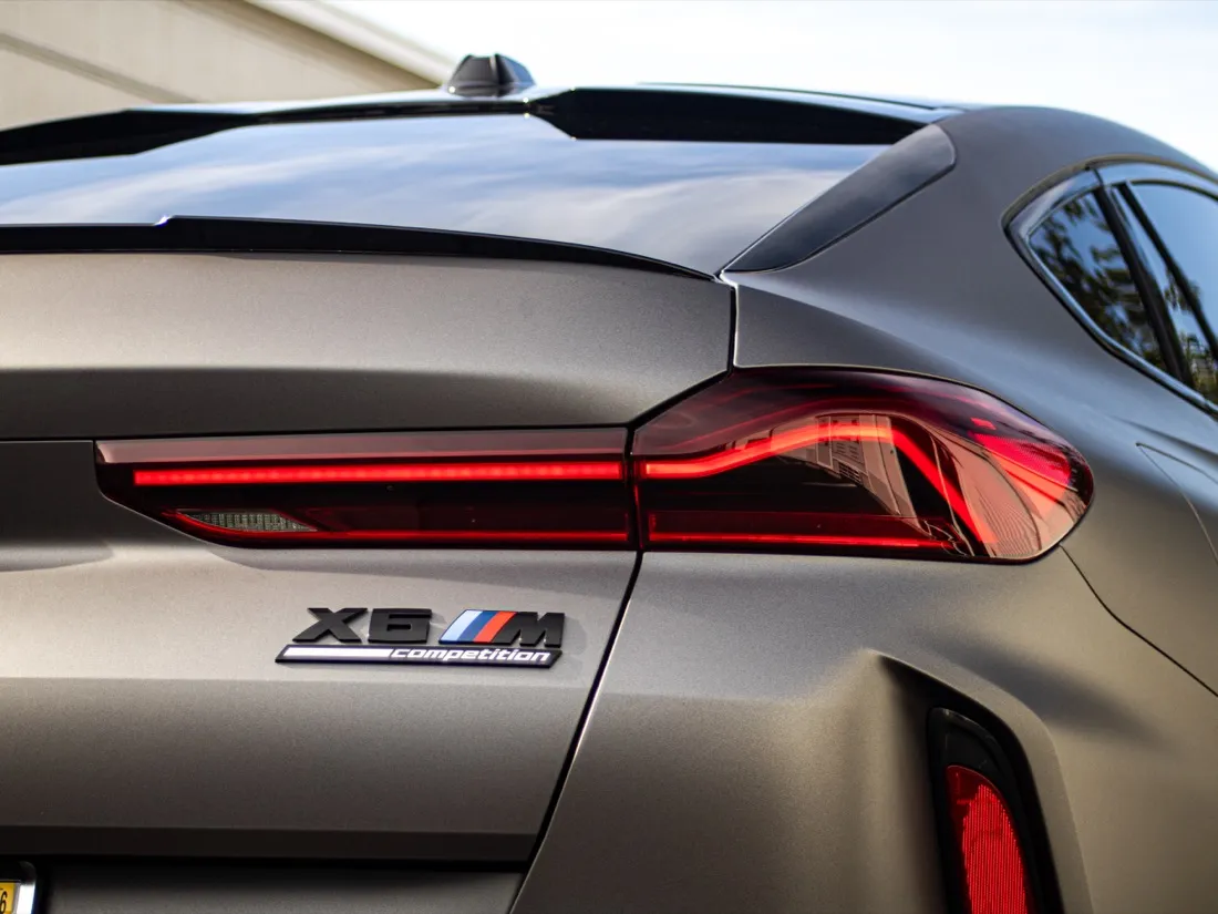 Rear quarter with the X6 M Competition badge over matte dark gray film