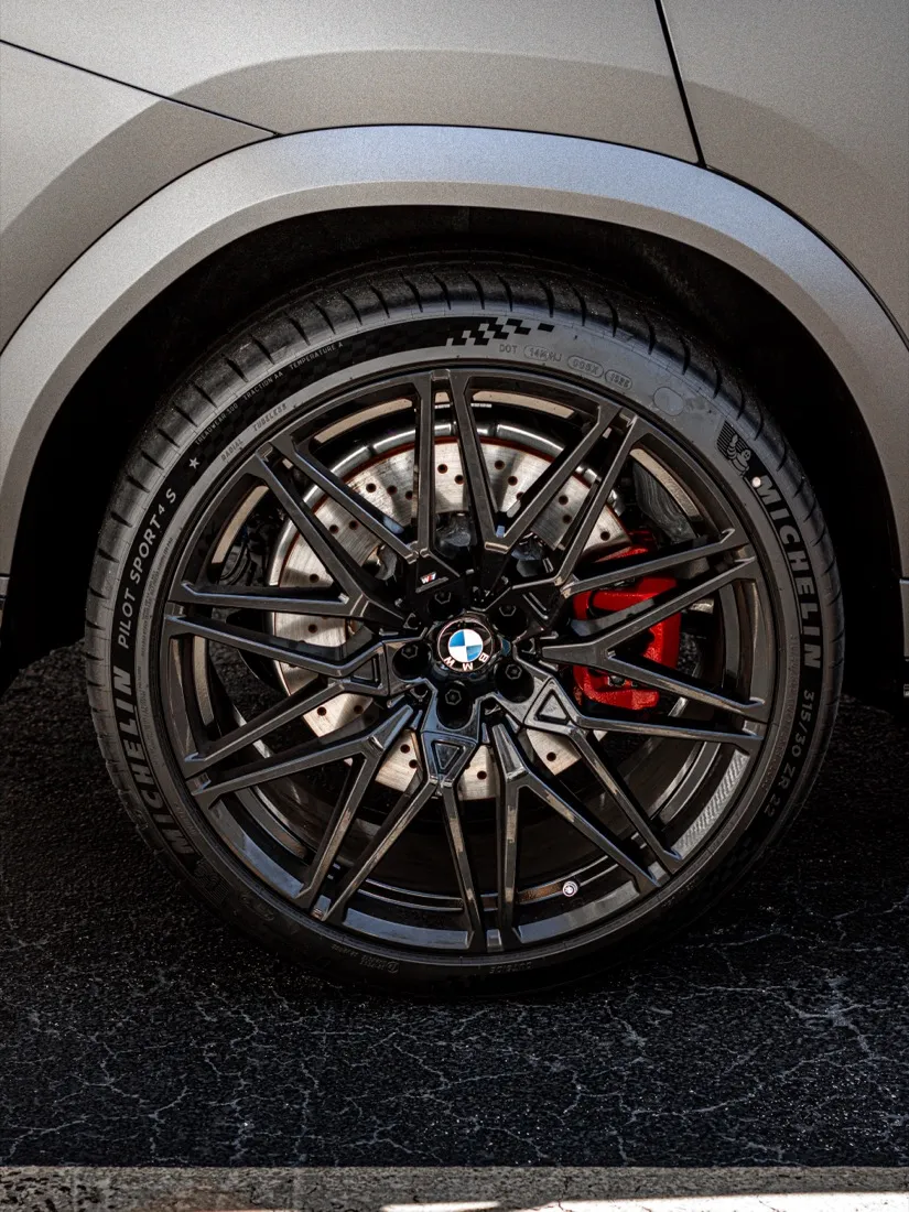 Black wheel and red M brake caliper against the matte dark gray wrap